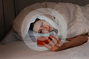 Young woman can`t sleep and using her smartphone in beg at night