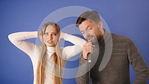 Young woman can`t take the noise of her boyfriend singing. Closing the ears with hands and making annoyed face