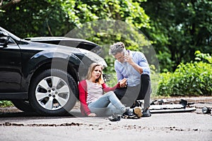 Young woman by the car after an accident and a man making a phone call.