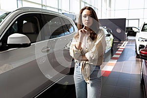 young woman in a car dealership showroom puzzled by the choice of a new car