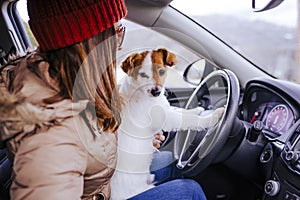 young woman in a car with her cute small jack russell dog. winter or autumn season