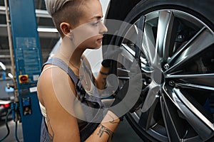 Young woman car mechanic works with a car wheel