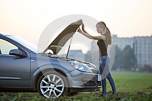 Young woman and a car with popped hood. Transportation, vehicles problems and breakdowns concept