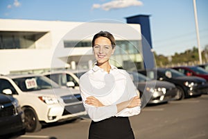 Young woman car rental in front of garage with cars on the background
