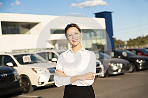 Young woman car rental in front of garage with cars on the background