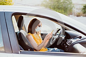 Young woman in a car using mobile phone, wearing protective mask. Summer season. prevention corona virus concept