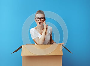 Young woman in cardboard box telling exciting news on blue