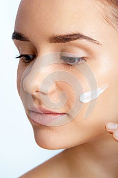 Young woman cares for face skin. Portrait of beautiful woman applying cream on face. Holding Moisturizing Lotion. Skin Care Concep