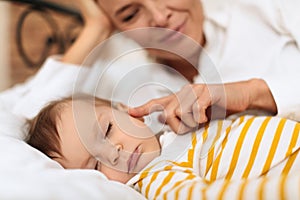 Young woman caressing her sleeping little baby girl, woman touching her kid cheek and smiling, enjoying sweet moment