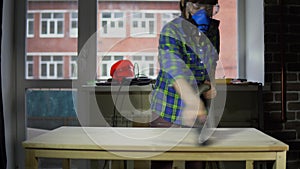 Young woman carpenter removes wood dust from countertop using vacuum cleaner.