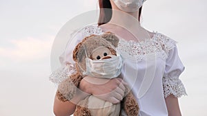A young woman carries her child s favorite toy. toy teddy bear in medical mask. girl carries in her hand toy teddy bear