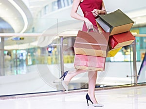 young woman carrying colorful paper bags walking in shopping mall