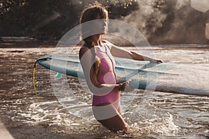 young woman carrying surfing board in hands while walking