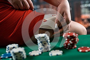 young woman in a casino in a red dress sits on a poker table with chips and cards