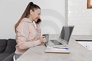 Smiling woman talking on smartphone while shopping online with a cup of coffee in her hand