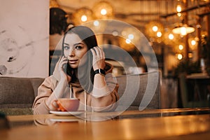 Young woman in casual clothes sitting at table in cafe, talking on cell phone.