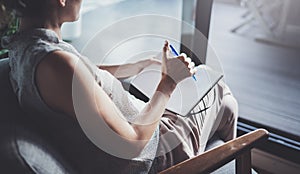 Young woman in casual clothes sitting at table in home and writing in notebook. Freelancer working home.