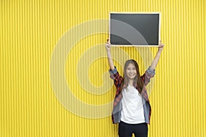 Young woman in casual show an empty blackboard on yellow wall with smiling