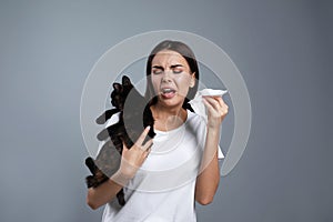 Young woman with cat  from allergy on grey background