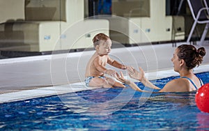 Young woman catching little son sitting poolside in swimming pool