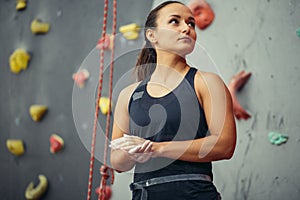Young woman with chalked hands posing at indoor climbing gym wall