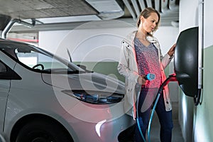 Young woman charging an electric vehicle in an underground garage