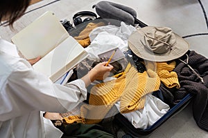 Young woman check baggage lists on notebook to prepare for traveling trip