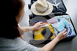 Young woman checking accessories and stuff in luggage at home before travel. Preparing suitcase for summer vacation trip