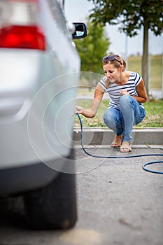 Young woman checking the car tyre pressure