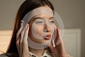 Young Woman Checking Her Facial Skin With Concern in a Brightly Lit Room photo