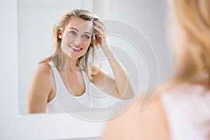 Young woman checking her hair in bathroom mirror