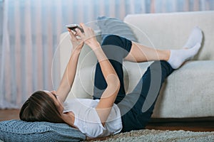 Young woman checking her smart phone lying on carpet