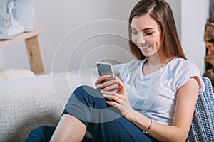 Young woman checking her smart phone sitting on sofa
