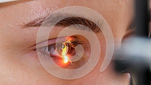 A young woman checking her visual acuity with a light of special big optometry machine - brown eyes color