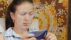 A young woman is checking messages on a mobile phone at home on the couch.