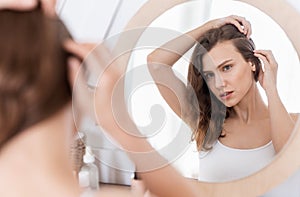 Young woman checking for thinning hair in mirror at home