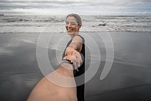 Young woman cheerfully grabbing a man's hand on the beach