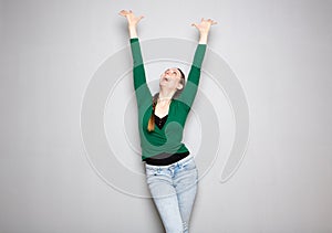 Young woman cheering with arms raised up against gray background