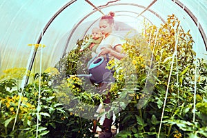 Young woman with child in her arms waters plants in greenhouse.