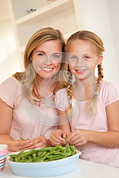 Young woman with child splitting pea in kitchen