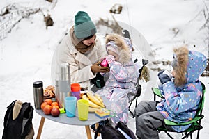 Young woman with children in winter forest on a picnic. Mother and two daughters