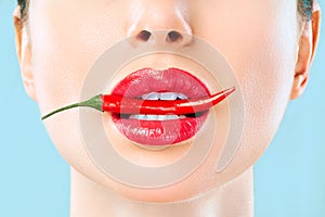 Young woman with chili red pepper isolated en blue background. Sexy female lips. Hot seductive girl