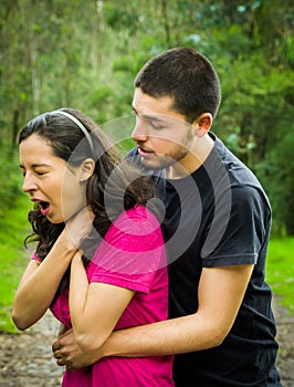 Young woman choking with man standing behind performing heimlich maneuver, park environment and casual clothes photo
