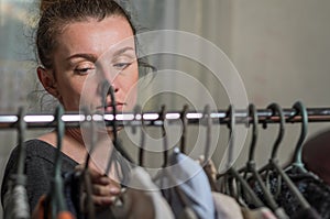 A young woman chooses clothes on hangers during shopping