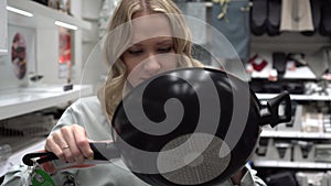 Young woman chooses a frying pan and utensils in a home goods store