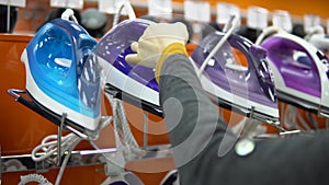 A young woman chooses an iron in a home appliance store.