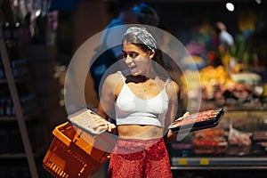 Young woman chooses meat in a grocery store