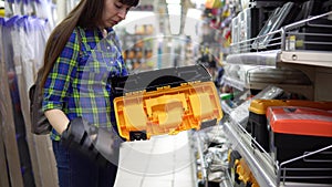 A young woman chooses a plastic tool box in the store.