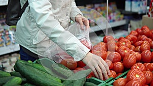 Young woman chooses ripe red tomatoes buying fresh vegetables in a supermarket