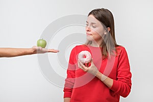 Young woman choosing between apple and donut